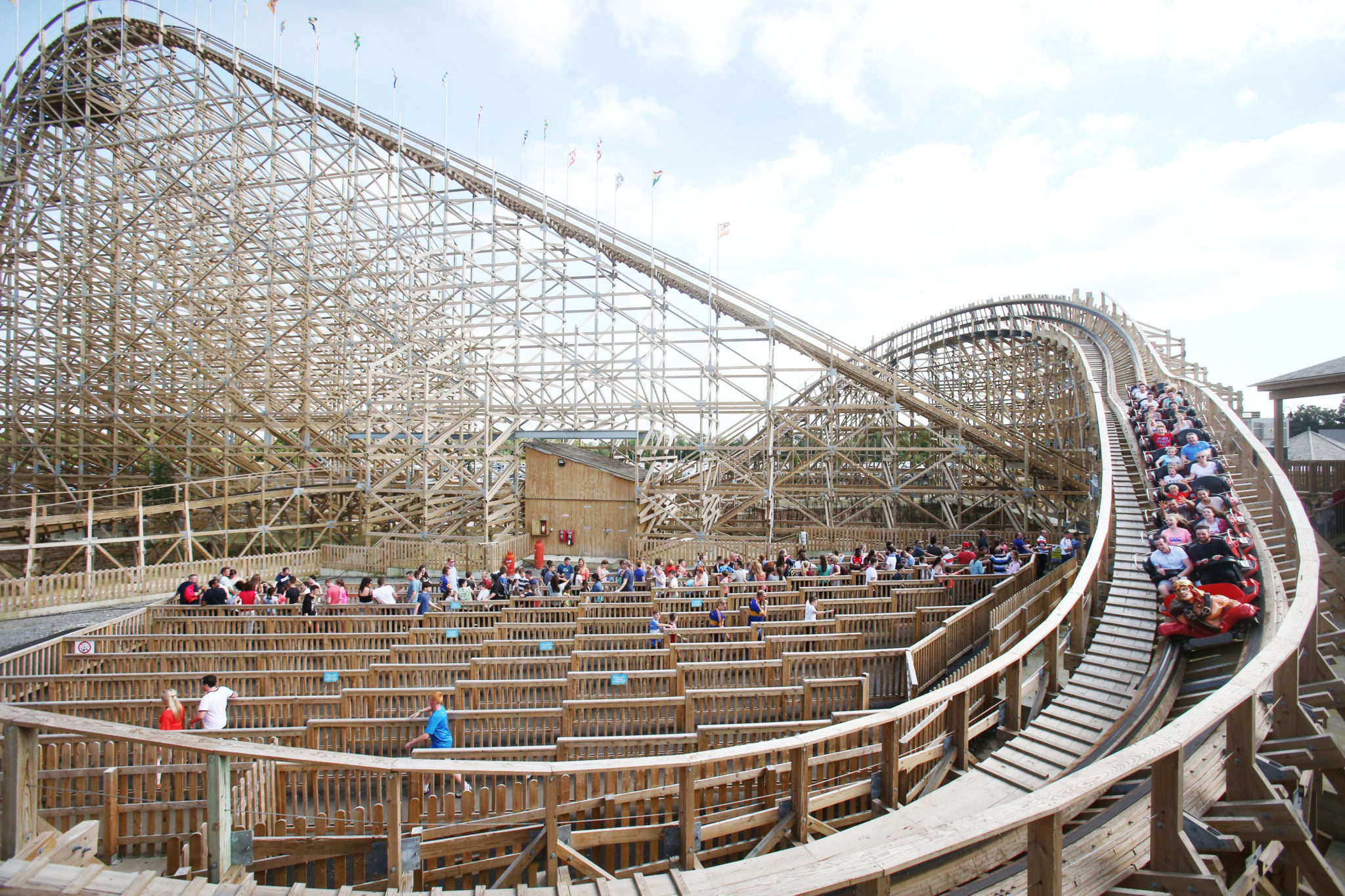 Wooden rollercoaster with people queueing to get on below